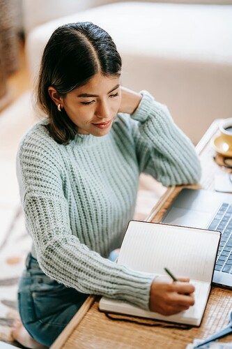 Latin American woman taking notes in notebook near netbook.